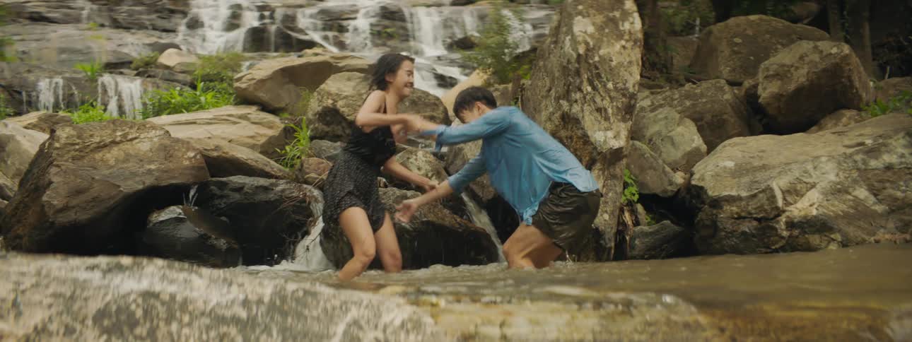 Man and woman play in pool at base of waterfall
