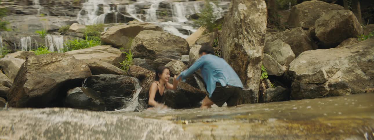 A young man and woman in a river splash one another and laugh and wrestle