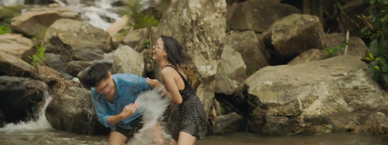 A man and a woman playing in a river splashing water at each other