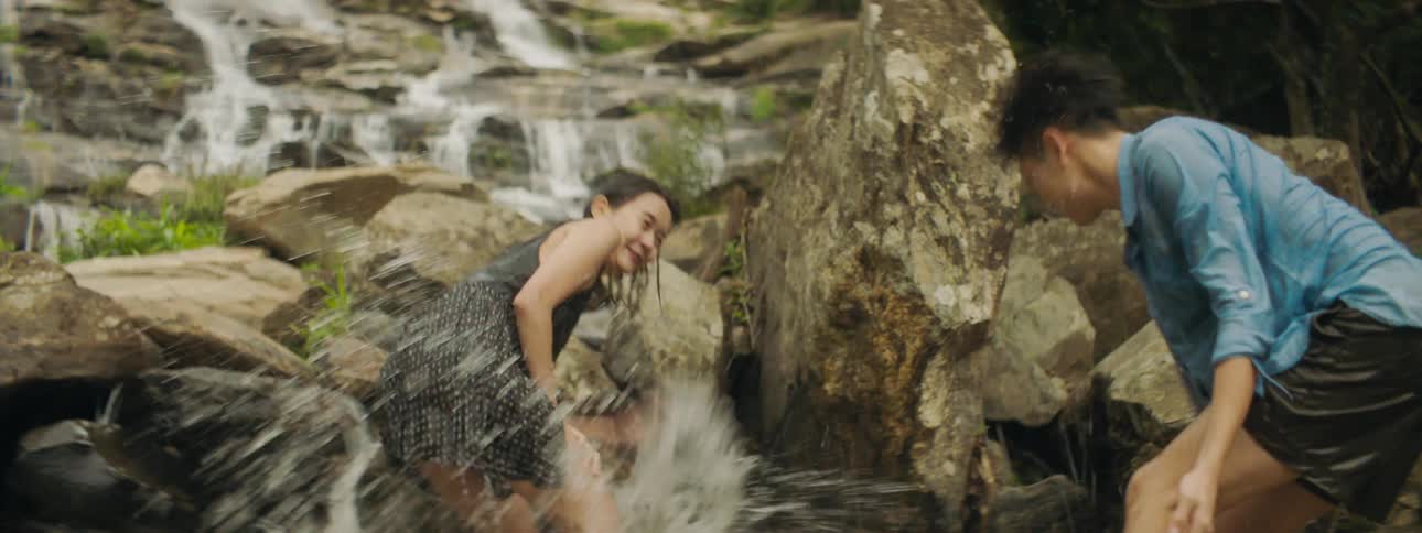 Two teenagers in a river laugh as they splash water at one another