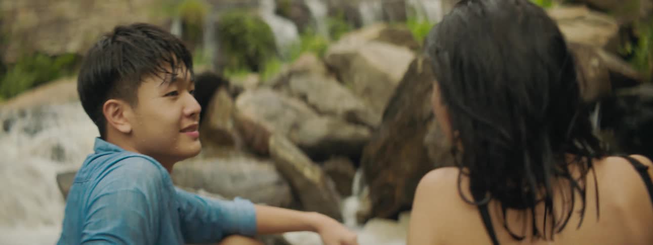 A man and woman sitting at a river talk and laugh together