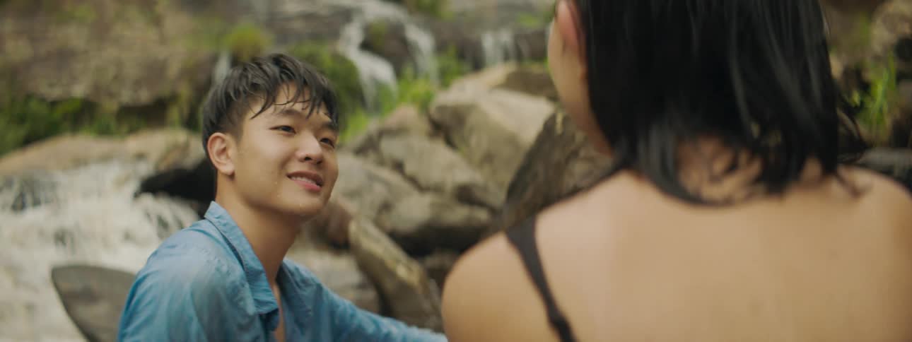Boy strokes girls wet hair as they look toward waterfalls flowing down large boulders