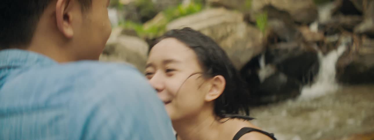 A young woman standing in a river kisses a man