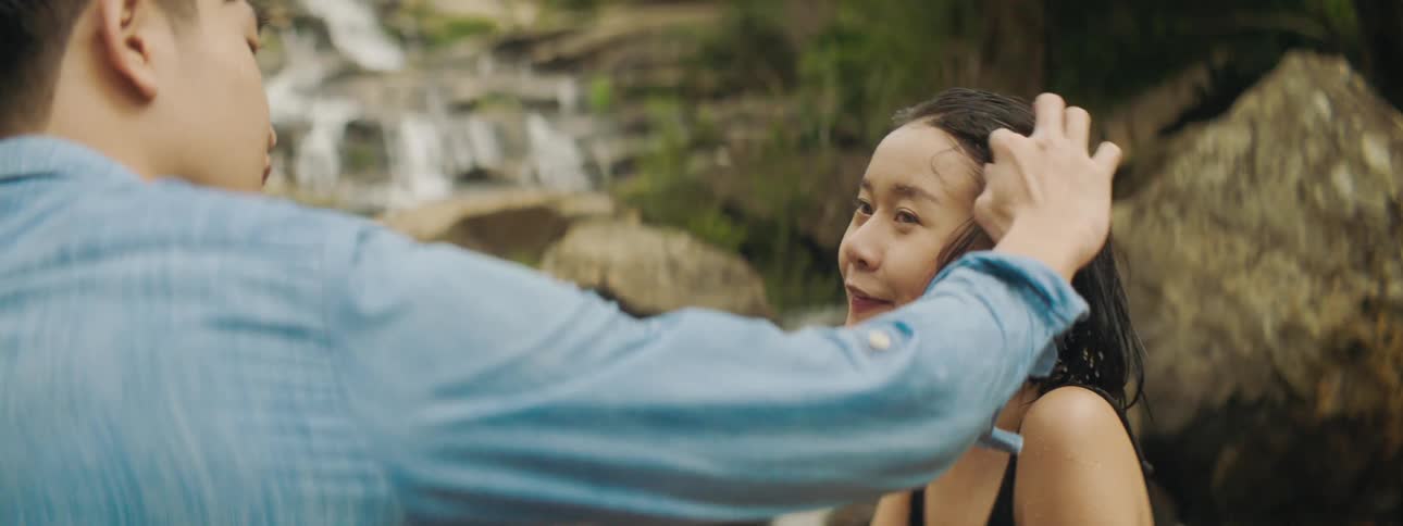 Couple standing besides a small waterfall one is wet from the water the other moving there hair