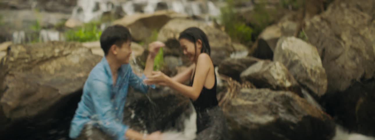 A man and woman laugh as they stand in river and splash one another