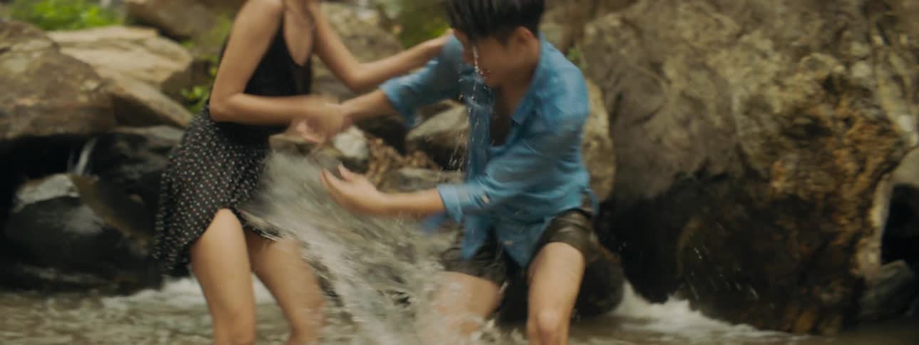 A teenage boy and girl in the river splash one another and laugh