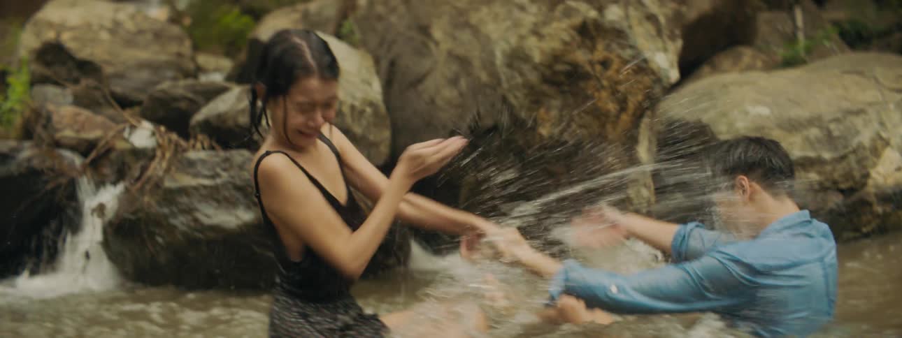 A young man and woman splash each other with water while playing in a river