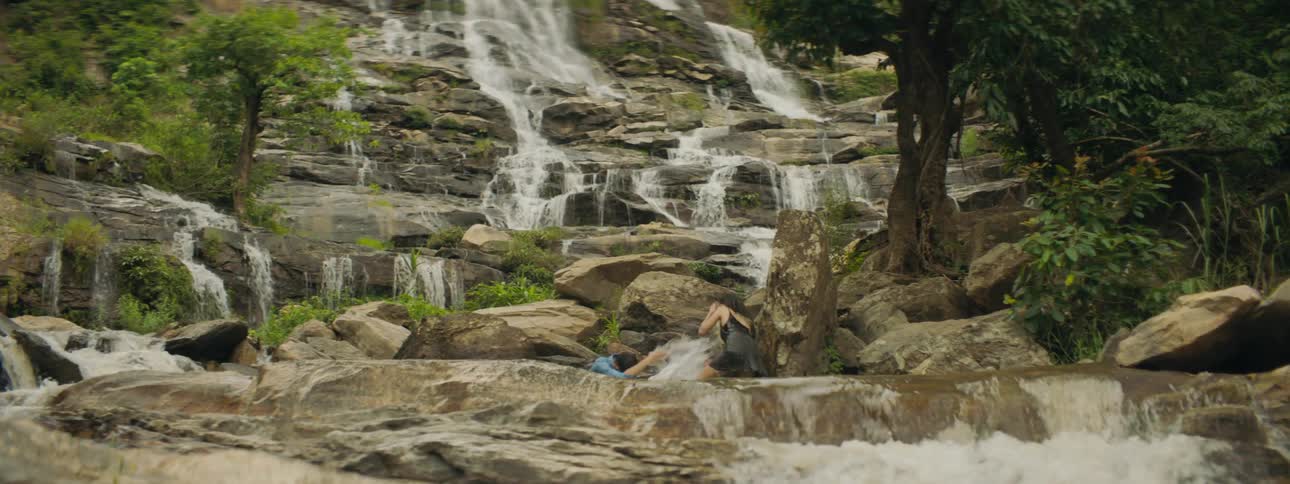 A man and a woman playing in a river splashing water at each other