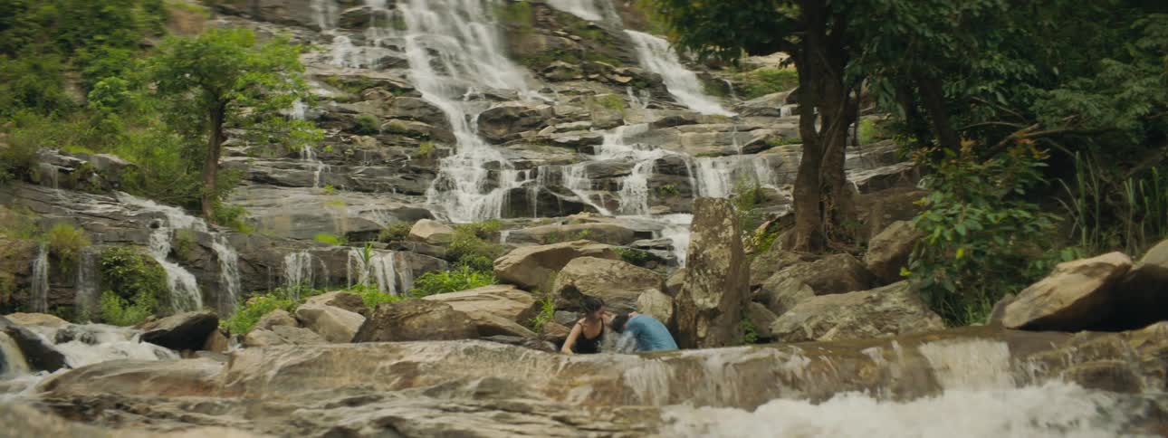 Two people are playing in the water by the waterfall