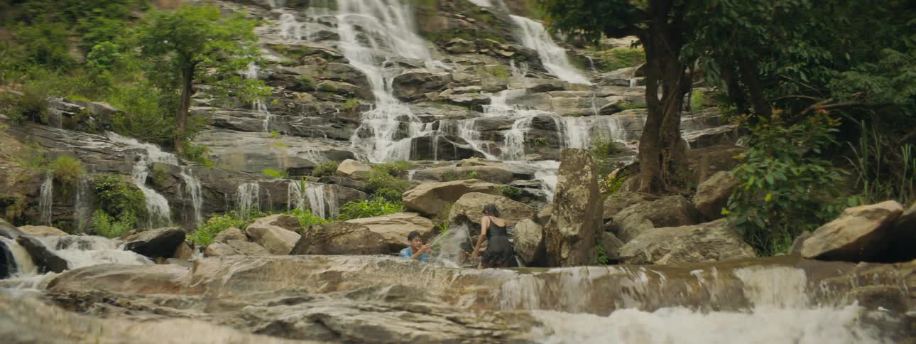 Man and woman play in water of waterfall flowing down terrace stone