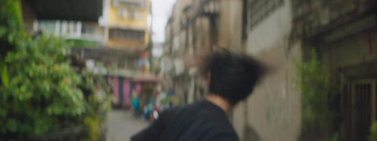 A young man looks into the camera while performing a pop dance in the alleyway of a city during the day