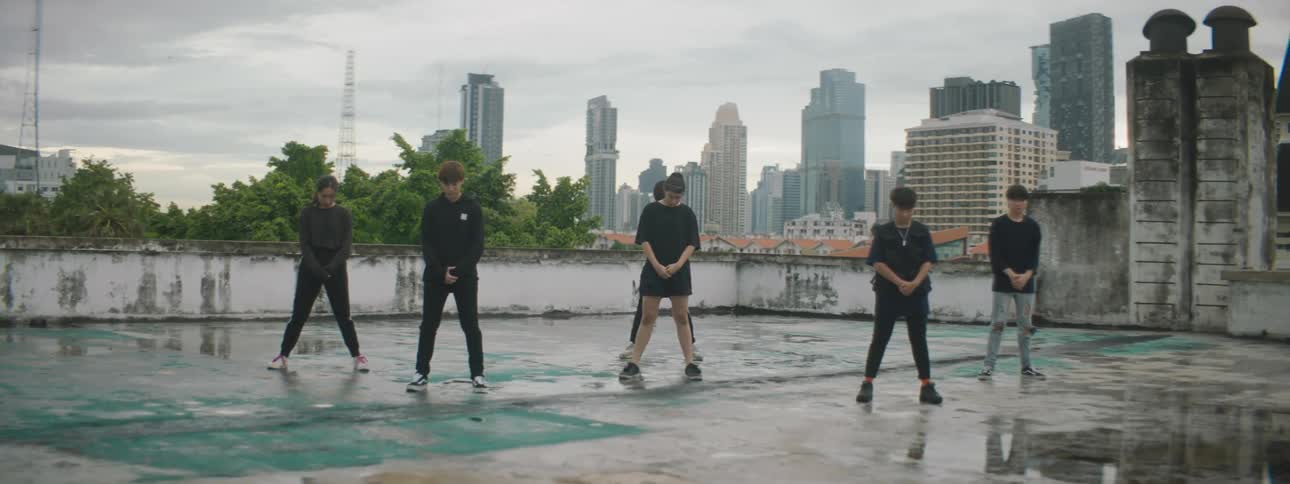 Group of people stand on concrete near puddle with skyscrapers in background