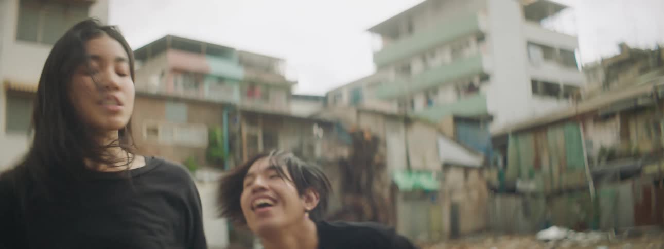 A young woman and man perform a dance in the slums of a city during the day