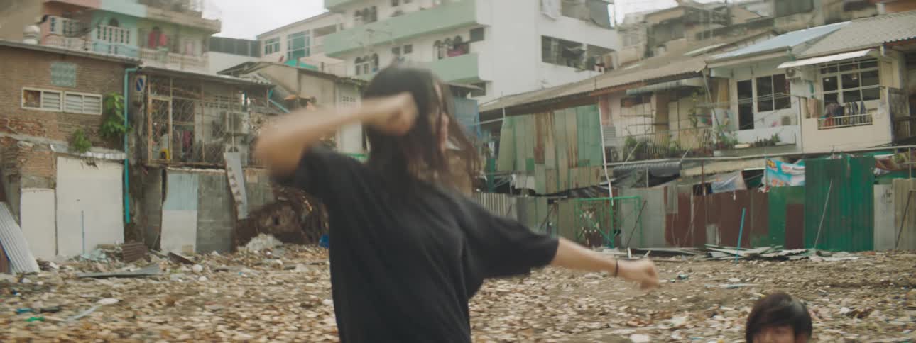 A young woman and man perform a pop dance in the slums during the day