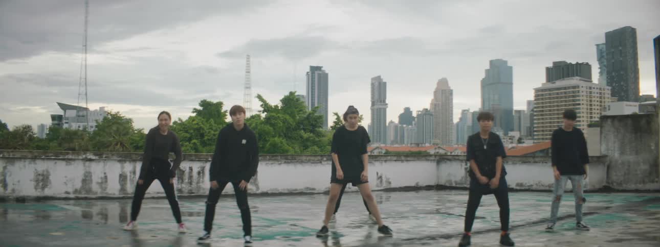 Dance troupe dances on wet roof with city skyline in background