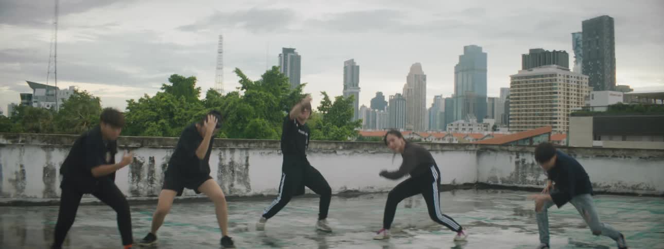 Men and women dancing on a rooftop with buildings the sky and clouds in the background