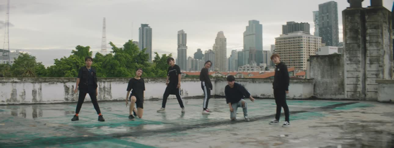 Male dancers perform routine near reflective puddle with mist covered city skyscrapers in background