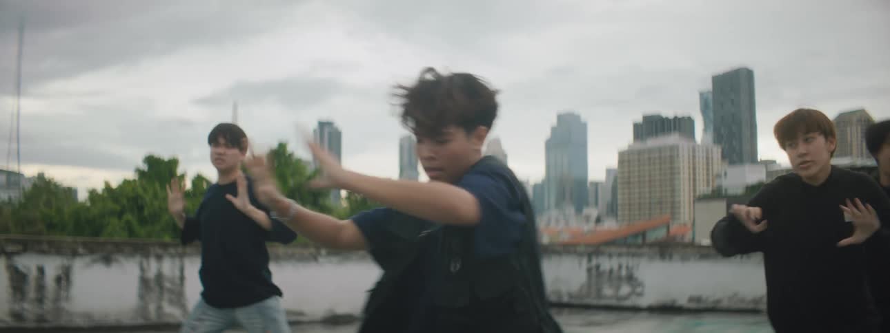 Teenagers perform a choreographed dance on a building rooftop with views of downtown