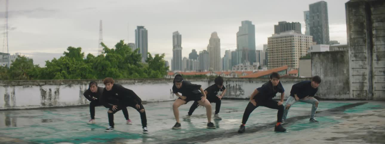 A group of teenagers dance outdoors on with a city skyline in the background