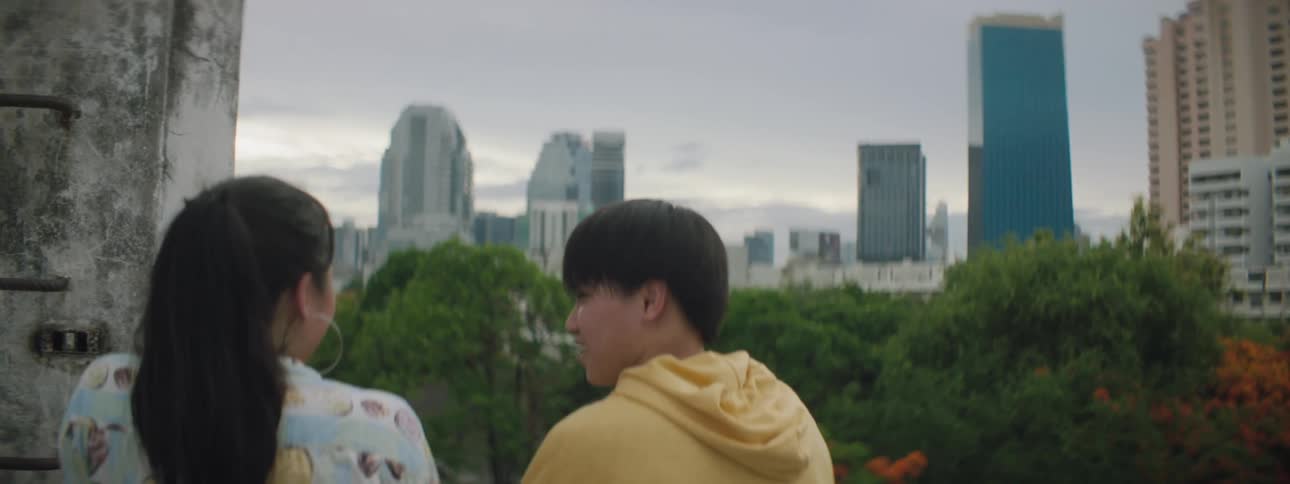 Man and woman talk near wall across park from downtown skyscrapers