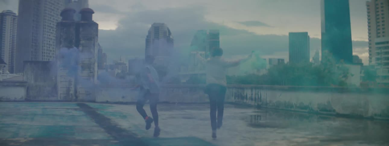 Two teenagers running on a rooftop holding containers with colored powder coming out of them