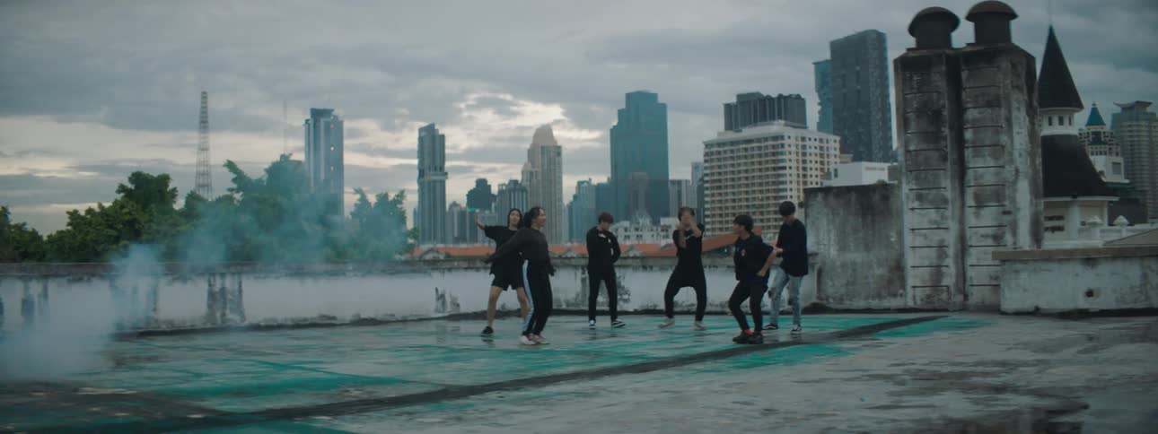 Men and women dancing on a rooftop with buildings the sky and clouds in the background