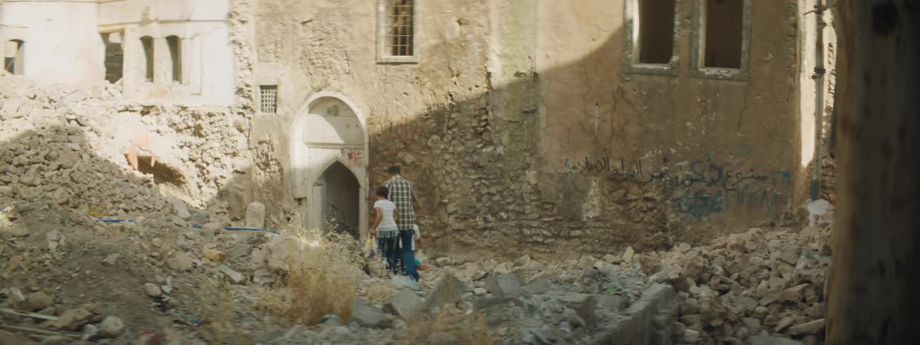 A man holding hands and walking with two girls holding bags with a building in the background