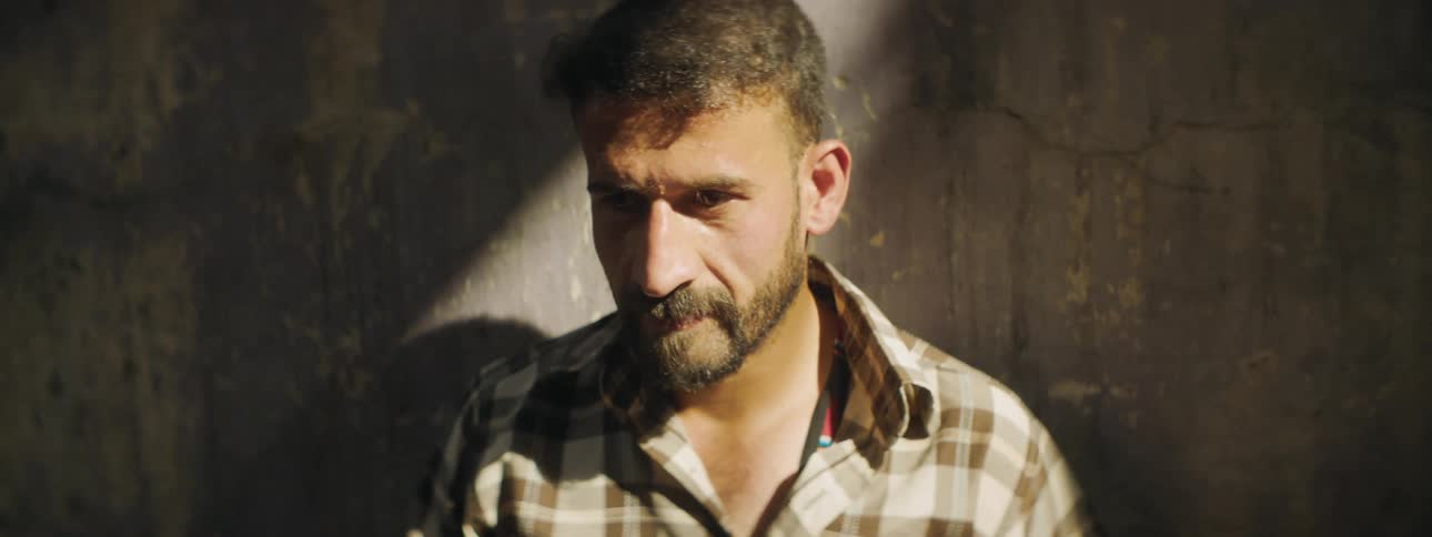 Man with a beard and a shirt leans against the wall in the sunlight