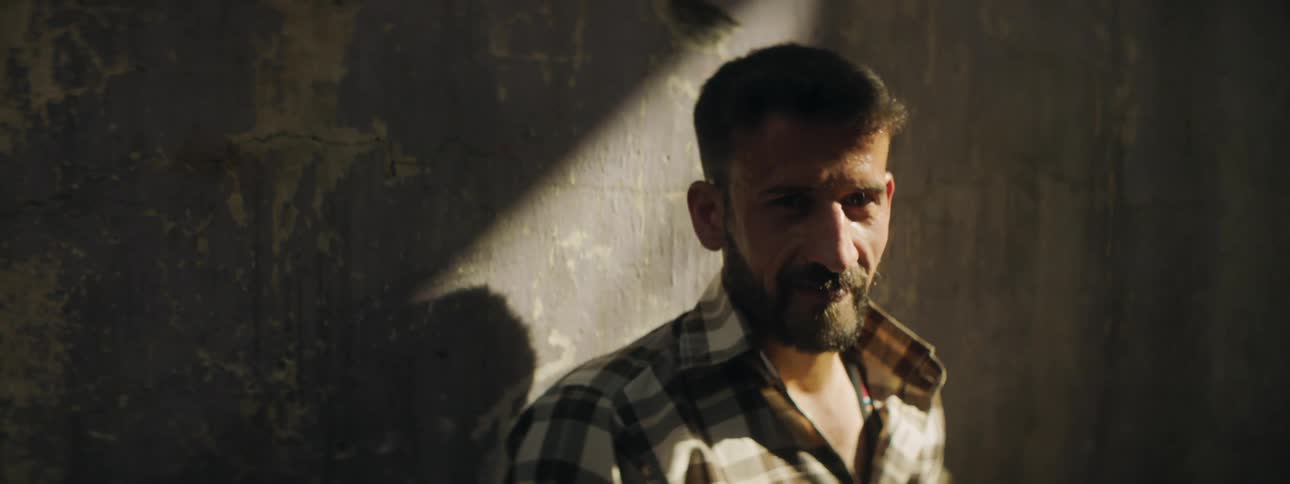 A man standing and staring with sunlight on his face and a wall behind him