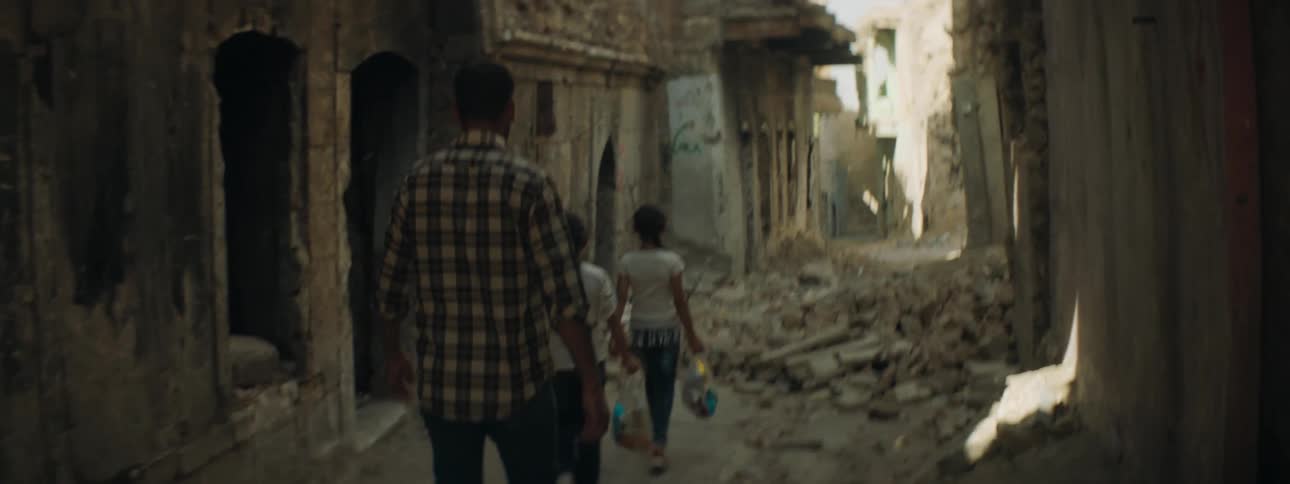 Father escorts daughters through archway down narrow rubble strewn street between ruined buildings
