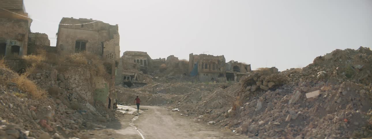 A person is walking into the ruined city