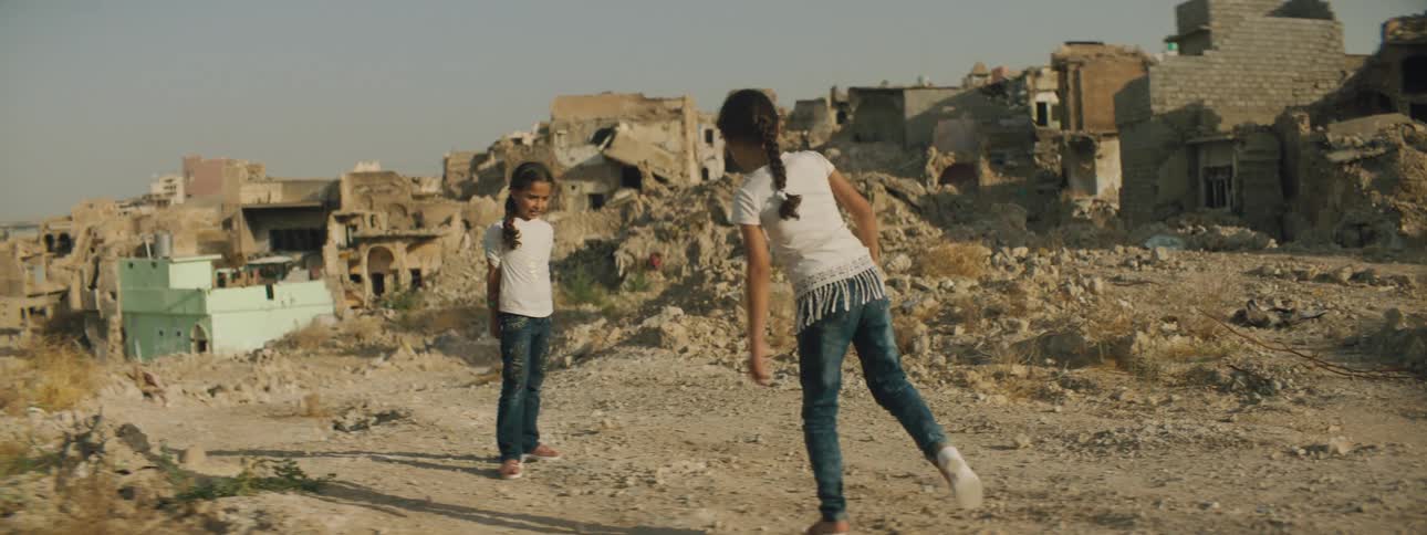 Two small girls play together amongst destroyed buildings and rubble