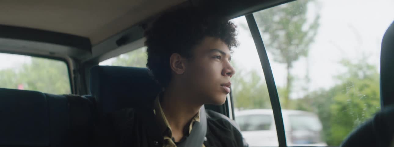 Teenage boy looks out the side windows of a moving car in the city streets