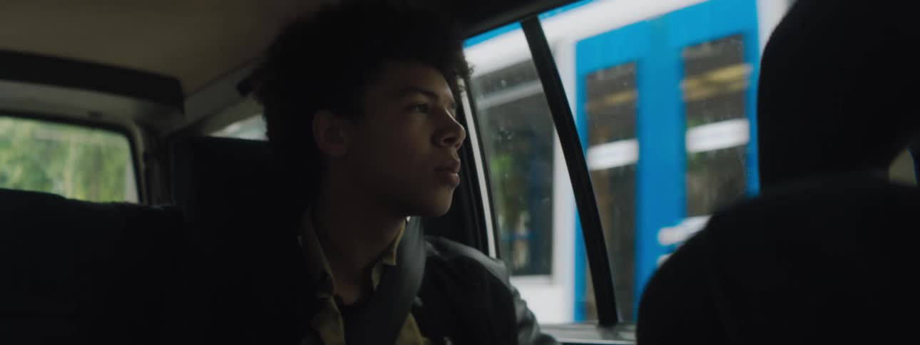 Teenage boy looks out the side windows of a moving car in the city streets