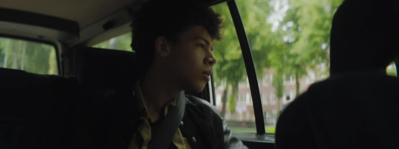 A teenage boy sitting in the backseat of a car looks out the window