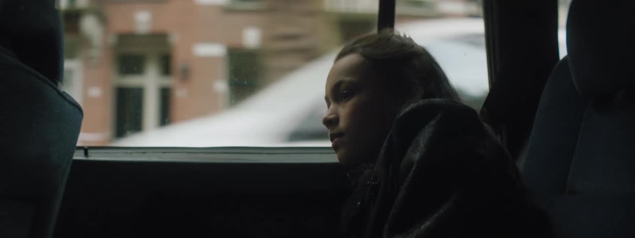 Girl sitting in the back seat of a car driving on city streets is silhouetted