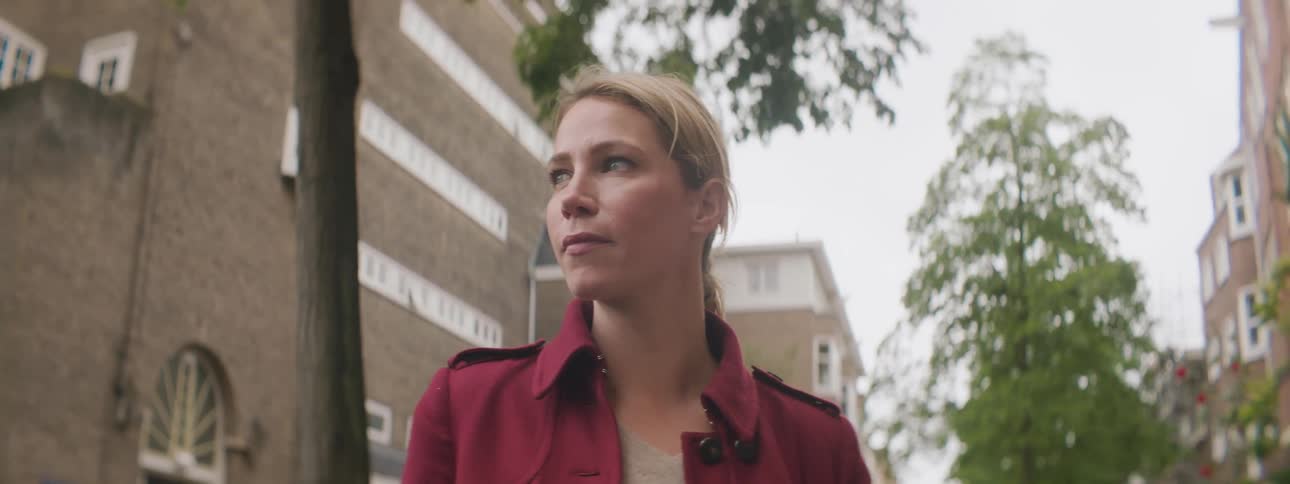 Blonde woman with a ponytail and a red jacket stands and looks around in the street