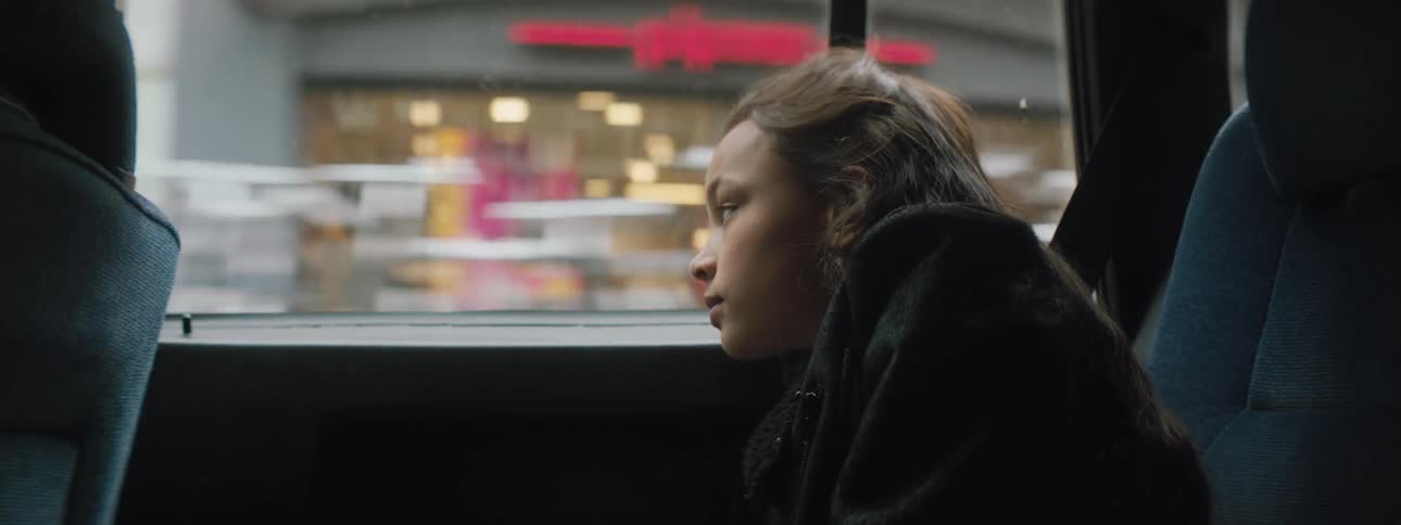 Girl looks out the car window of a moving car in the city streets