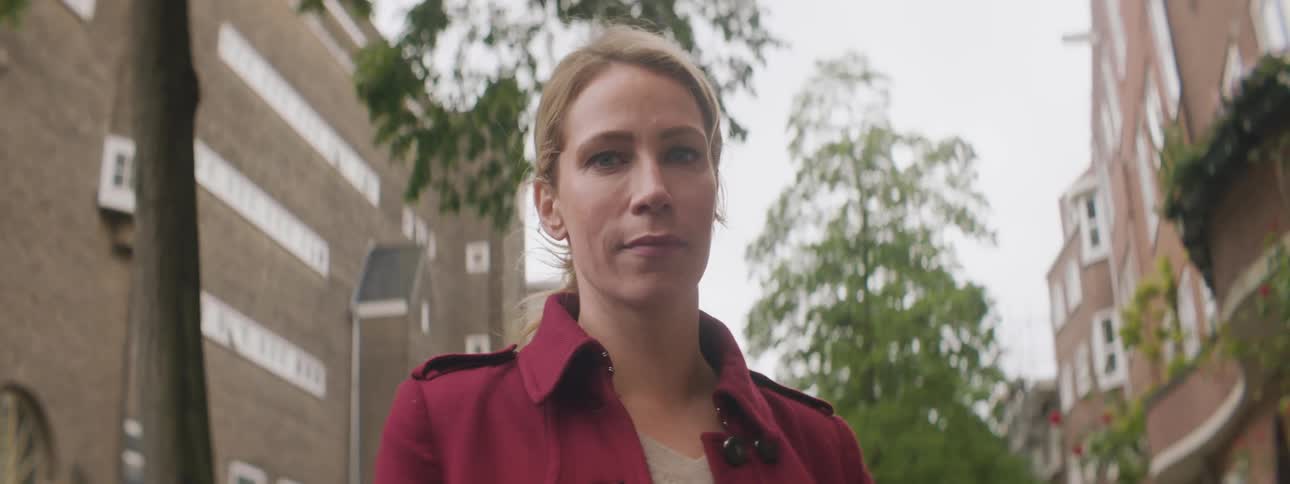 A woman standing and staring with trees buildings the sky and clouds in the background