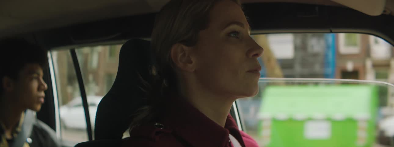 A woman driving down a city street with her teenage son in the back seat