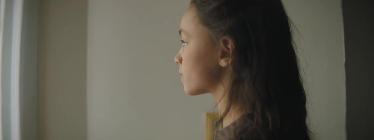 A young girl at home looks at a cell phone and then out the window