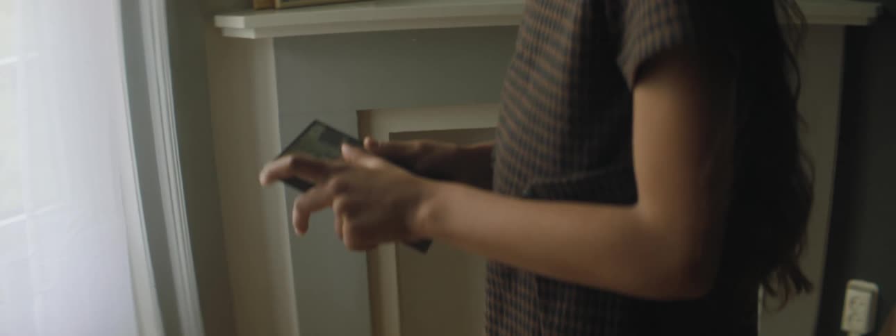 A young girl runs through a house and picks up a cell phone and rubs the screen on her dress