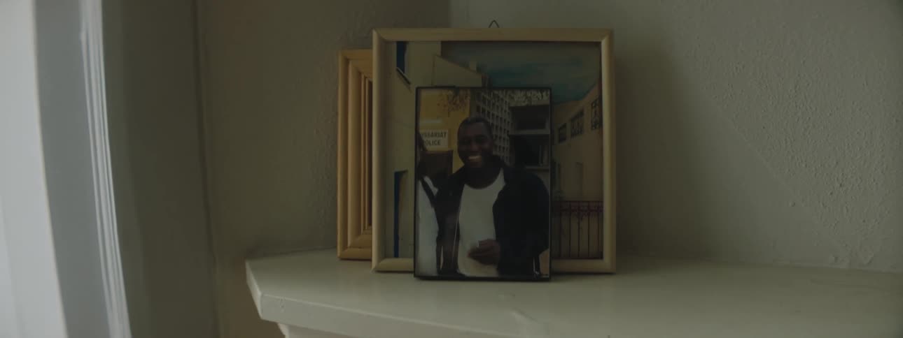 A man smiles in a photo on a shelf in a home decorated with framed art