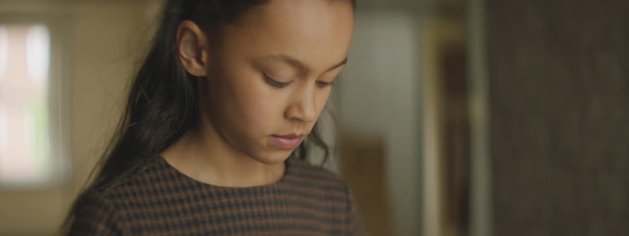 A girl in a room looking down then running through a doorway with a window in the background