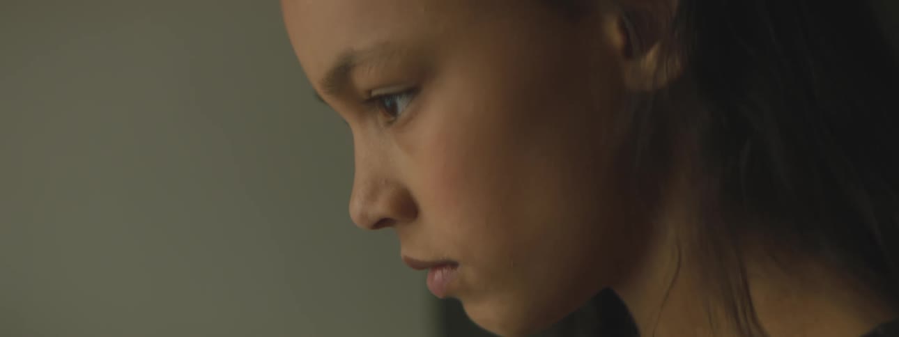 Side view of a girl with dark brown hair looking down in a room