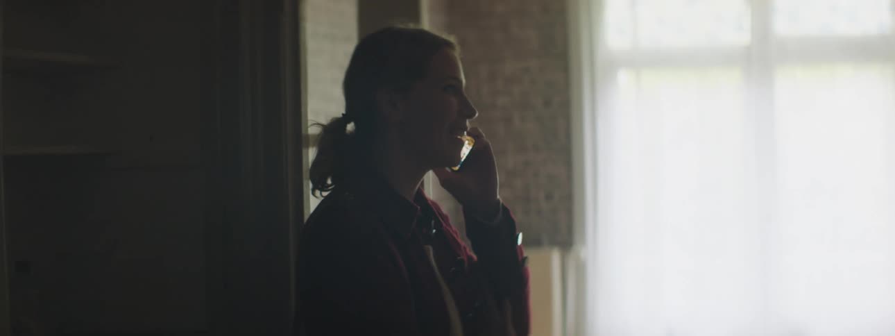 Woman stands in shadowed room then makes call on mobile phone and starts laughing