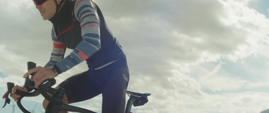 A man wearing a helmet and sunglasses is riding a bike under a cloudy sky