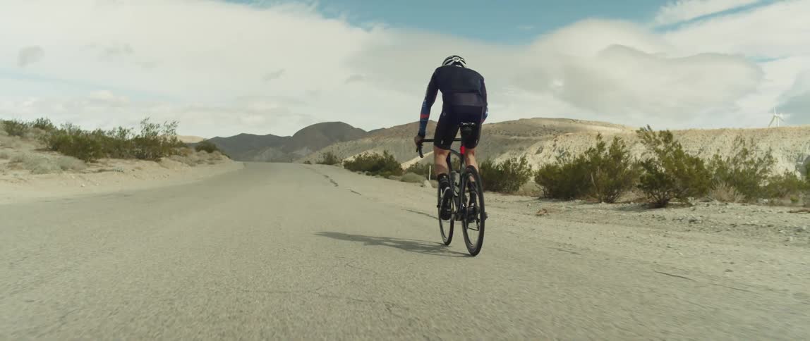 Man wearing a helmet rides a bicycle on a road in the desert close to the mountains