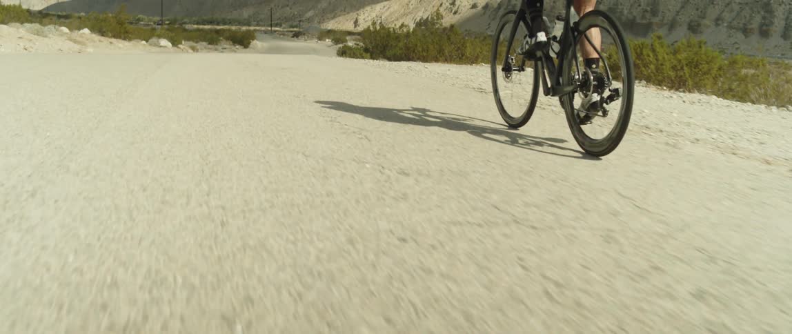 A man wearing a bicycle helmet is riding a bike on a road near mountains