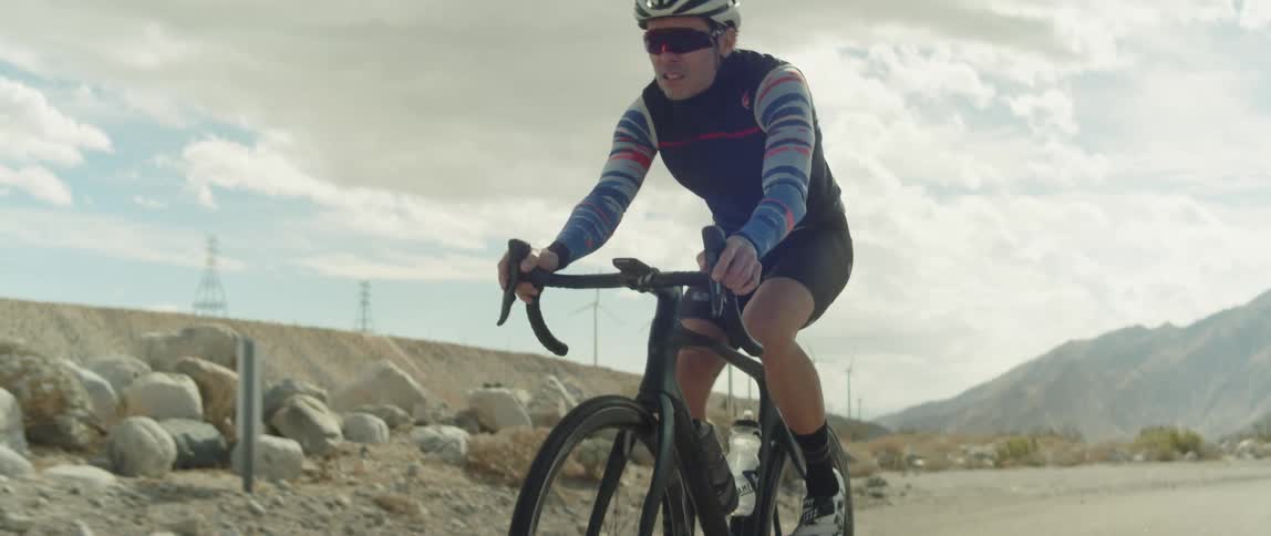A man is cycling on a road in the desert on a cloudy day